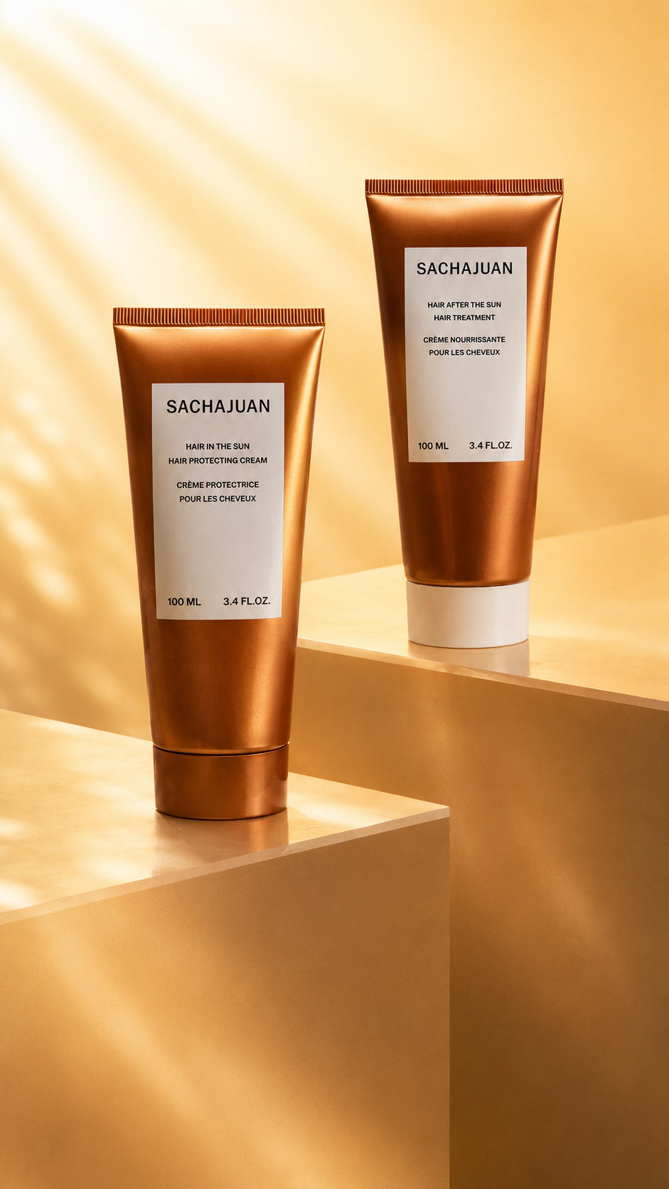 Two Sachajuan hair care tubes, one of the Hair In The Sun and one of the Hair After the Sun Hair, displayed on a geometric gold pedestal.